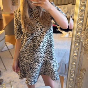 Leopardmönstrad kortklänning volang hm trendig  - Säljer en kort klänning med leopardmönster i svart och beige. Klänningen har korta ärmar och en lös passform med lätt volang nertill. Perfekt för dig som gillar djurmönster och vill sticka ut.