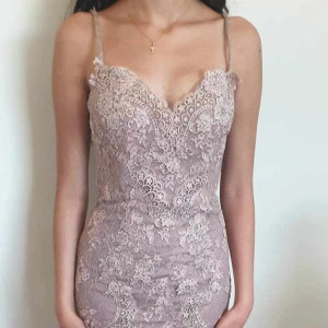 Ljuslila spetsklänning med smala axelband - Elegant långklänning i ljuslila med vacker spets och smala axelband. Klänningen har djup v-ringning fram och öppen rygg, samt figurnära passform. Perfekt för bal eller festliga tillfällen. Den är även kemtvättad. Storlek 38 men passar till storlek 36. Pris kan diskuteras.
