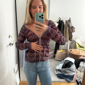 Missoni kofta - Säljer en snygg kofta i lila och vinröda toner med vitt sicksackmönster. Koftan har två fickor och långa ärmar. Perfekt att slänga på sig till jeans för en chill look.