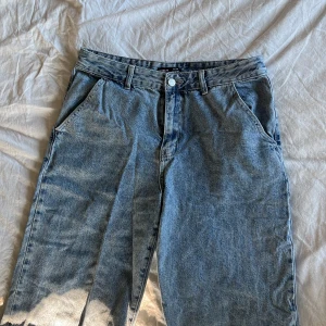 Blå wide leg jeans från SHEIN - Säljer ett par blå jeans från SHEIN med wide leg-passform och råa kanter nertill. Jeansen har klassisk femficksdesign, bälteshällor och stängs med knapp och dragkedja. Perfekta för en avslappnad stil.