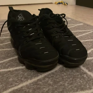 Svarta Nike Air Vapormax sneakers - Svarta Nike Air Vapormax sneakers med helsvart ovandel och svarta snören. Skorna har en unik, bubblig sula och diskreta vita detaljer på ovandelen. Perfekta för dig som gillar sportig och modern stil.