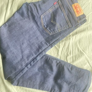 Levi's 513 blå jeansbyxor - Säljer ett par klassiska blå Levi's 513 jeans med raka ben och normal passform. Byxorna har fem fickor, dragkedja och knapp i midjan samt tydliga Levi's-detaljer som röd etikett och läderpatch bak. Perfekta till vardags!