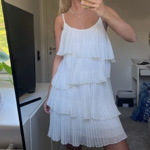 Student klänning - Säljer en superfin vit klänning med flera lager volanger och plisserat tyg. Klänningen har smala axelband och är ärmlös, perfekt för sommarens alla tillfällen. Lätt och luftig modell med vacker rörelse i tyget.