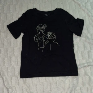 Svart t-shirt med linjeteckning - Svart t-shirt med ett stilrent tryck av två personer i linjeteckningsstil på bröstet. Enkel och modern design som passar till många outfits. Mjuk och bekväm bomullskänsla.