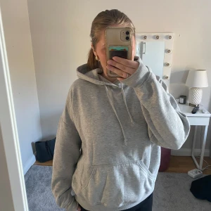 Grå hoodie med ficka - Säljer en klassisk grå hoodie med huva. Tröjan har en stor magficka och ribbade muddar vid ärmslut och nederkant. Perfekt för en avslappnad stil. Hoodien har små märken av att den är använd men inget större som syns!
