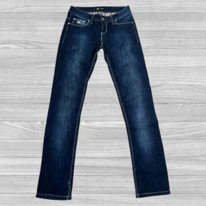 Burberry jeans - Snygga mörkblå jeans från Burberry med klassisk gul broderad logga på fickan och ikoniskt rutigt innerfoder i midjan. Jeansen har raka ben och kontrastsömmar, samt detaljer med knappar och dragkedja framtill.