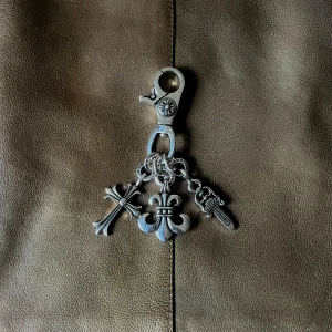 Rockstar Chrome Keychain - Nyckelring med kraftfulla detaljer: ett kors, ett Fleur de Lis-motiv och ett ornamenterat svärd. Perfekt för en rockig eller gotisk stil med attityd. Mörk silverton. Unisex