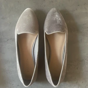 Gråa ballerinaskor i sammet - Säljer ett par stilrena gråa ballerinaskor i mjuk sammet med spetsig tå. Skorna har en klassisk och enkel design utan extra detaljer, perfekt för dig som gillar en minimalistisk look.