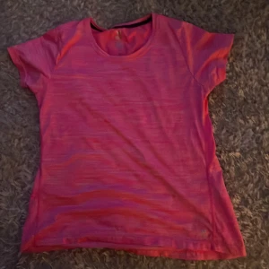 Rosa tränings-t-shirt - Säljer en rosa t-shirt perfekt för träning. T-shirten har rund halsringning och är kortärmad med lätt och luftig känsla. Materialet är syntetiskt och snabbtorkande, vilket gör den optimal för aktiva dagar.