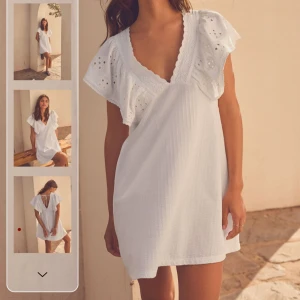 Vit kortklänning med broderade volangärmar - Superfin vit kortklänning med v-ringning och broderade volangärmar. Klänningen har knyt i ryggen och är tillverkad i ett lätt och luftigt material, perfekt för sommaren eller student!