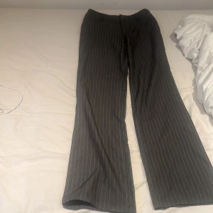 Grå randiga kostymbyxor från Madlady - Säljer ett par grå kostymbyxor från Madlady med vita tunna ränder. Byxorna har en rak och lite vidare passform. Perfekta för en stilren look. ( sista bilden är byxorna ut och in) ( allt som är andvänt kommer tvättas innan köp)