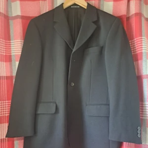 Svart kavaj från Batistini - Klassisk svart kavaj från Batistini med enkelknäppning och två fickor med lock framtill. Kavajen har en stilren design och är perfekt för mer uppklädda tillfällen.