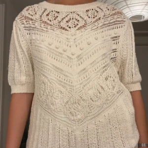 Vit stickad blus från Zara - Superfin vit stickad blus från Zara med korta ärmar och rund hals. Blusen har ett detaljerat virkat mönster och små bollar i stickningen, vilket ger en bohemisk och trendig vibe. Perfekt till jeans eller kjol för en chill look.