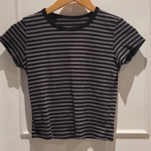 Randig svart och grå t-shirt - Säljer en kortärmad t-shirt med svarta och grå horisontella ränder. T-shirten har rund halsringning med svart kant och är i mjuk bomull. Onesize men är som XS-S. 