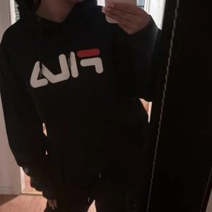 Svart FILA hoodie med logga - Säljer denna svarta FILA hoodien i storlek M, den är i bra skick men har använts flertal gången. Den är jättebekväm och snygg på säljer pga att den inte kommer till användning💞