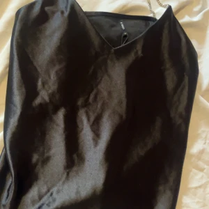 Svart satin klänning med strassband - Supersnygg svart klänning från ONLY i satin med glansig finish. Klänningen har smala axelband i strass som ger en lyxig känsla och v-ringad hals. Perfekt för dig som vill sticka ut med en elegant och trendig look.