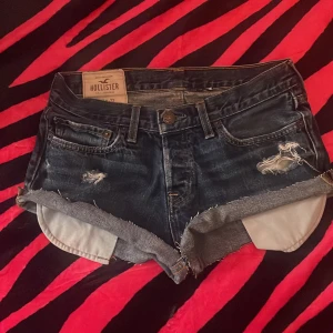 Mörkblå jeansshorts från Hollister - Snygga shorts från hollister i storlek w30❤️lågmidjade och korta! Kan behöva sys på kanten men funkar att använda ändå såklart! Hålen ingår i designen❣️💕knäpps med knappar där fram❤️