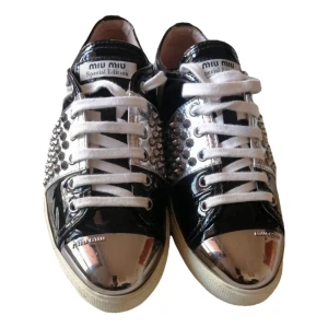 Miu Miu Special Edition sneakers silver - Unika Miu Miu Special Edition sneakers i svart och silver med coola nitar på sidorna och metallic-detaljer på tån. Skorna har vit snörning och platt sula. Tillverkade i skinn med glansig finish, perfekta för dig som vill sticka ut.