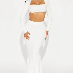 Vit långklänning med crop top-look - Supersnygg vit långklänning med figurnära passform och crop top-design. Klänningen har långärmad överdel med fyrkantig urringning och öppen rygg. Kjolen är högmidjad och slimmad hela vägen ner. Perfekt för dig som vill sticka ut med en modern och trendig look.