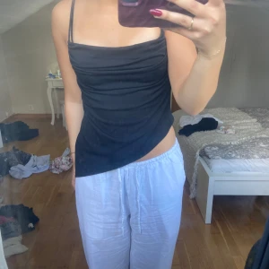 Svart asymmetrisk linnetopp från BikBok  - Svart linnetopp från BikBok i storlek XS med tunna axelband och snygg asymmetrisk nederkant. Toppen har draperad front och sitter figurnära, perfekt för en trendig look. 