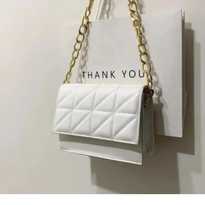 Vit quiltad axelväska med kedja - Snygg vit axelväska med quiltat mönster och guldig kedjerem. Väskan har magnetlås och plats för mobil, plånbok och småsaker. Perfekt accessoar för att lyfta din outfit med en stilren och modern touch.