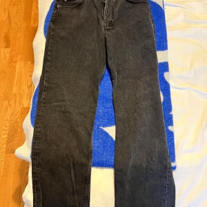 Svarta jeans från J.Lindeberg 33/34 - Säljer ett par svarta jeans från J.Lindeberg i klassisk femficksmodell. Jeansen har raka ben, snygga silverfärgade nitar och diskret logga vid fickan. Materialet är robust denim i bomull och passformen är normal. Perfekta för en clean och stilren look.