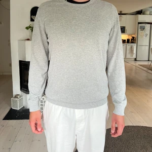 Bläck Tröja - En stilren ljusgrå tröja från Bläck i storlek XL. Tröjan har rund halsringning, ribbade muddar och är långärmad. Perfekt för dig som gillar en clean och enkel look. Materialet känns mjukt och passar till många outfits.