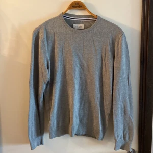 Grå stickad tröja från Pier One - En stilren grå stickad tröja från Pier One med rund halsringning och ribbade muddar. Perfekt för lager-på-lager och funkar till både jeans och chinos. Enkel design som är lätt att matcha och passar dig som gillar en clean look.