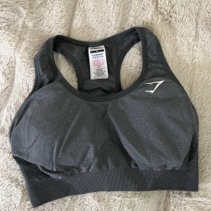 Mörkgrå sporttopp från Gymshark - Säljer en mörkgrå sporttopp från Gymshark med meshdetaljer och brottarrygg. Toppen har en tight passform och är tillverkad i ett stretchigt syntetmaterial, superskön. logga framtill och bak. 