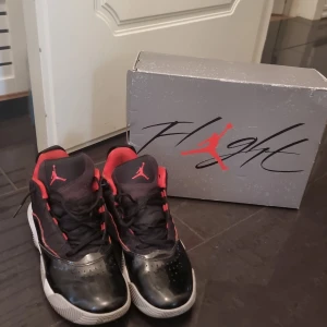 Jordan max aura 2 - Säljer ett par Nike Air Jordan max aura 2 i svart och rött med klassisk Jumpman-logga på plösen och sulan. Skorna har snörning, rund tå och en vit sula med tydligt mönster. Perfekta för dig som gillar streetstyle och vill sticka ut med ikoniska detaljer.