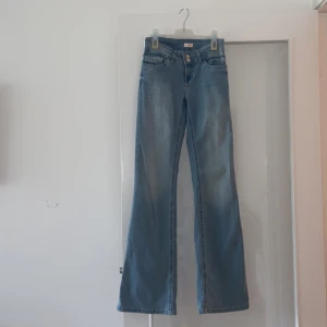 Ljusblå bootcut jeans från Nelly - Snygga ljusblå jeans från Nelly med bootcut passform och klassisk femficksdesign. Jeansen har dubbla knappar i midjan och coola röda broderier på bakfickorna. Perfekta för dig som gillar en retro vibe och vill ha ett par jeans som sticker ut.