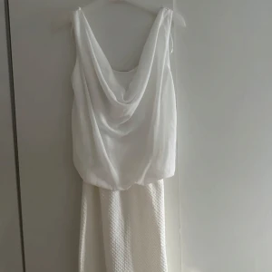 Vit klänning med draperad topp - Snygg vit kortklänning draperad topp i tunnare tyg. Kjolen har en strukturerad, vävd känsla som ger extra detalj. Perfekt för dig som gillar stilrena och fräscha looks. Ärmlös modell med djupare ringning både fram och bak