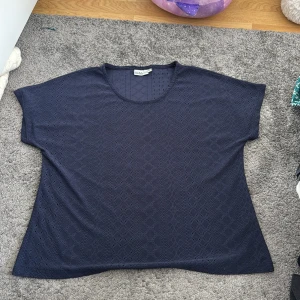 Mörkblå blus från Isolde i spets - Säljer en mörkblå blus från Isolde med korta ärmar och rund halsringning. Blusen har ett snyggt spetsmönster med små hål och geometriska detaljer