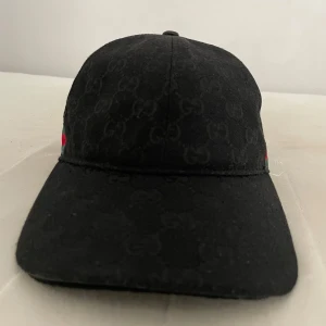 Svart keps - Snygg svart keps med klassisk böjd skärm och ikoniska gröna och röda ränder på sidan. Tillverkad i bomullsmaterial som känns både lyxigt och bekvämt. Perfekt accessoar för att lyfta din streetwear-look. Lappen är trasig men ska inte va några andra problem.