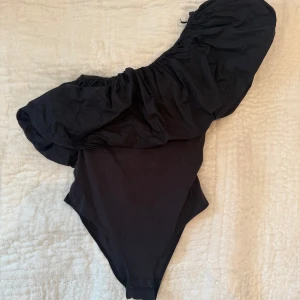 Svart offshoulder topp från H&M XS - Supersnygg svart offshoulder topp från H&M i storlek XS. Toppen har en dramatisk puffärm på ena sidan och är figurnära i modellen. Perfekt för dig som vill sticka ut med en cool och trendig look.