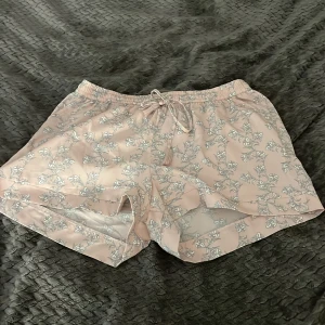 Blommiga ljusrosa shorts Angelolog XS - Supersöta ljusrosa shorts från Angelolog i storlek XS. De har ett vitt blommigt mönster, elastisk midja med snörning och är tillverkade i ett lätt och svalt material. Perfekta för varma dagar när du vill ha en chill och trendig look. Skulle mer säga att de är en S o kanske passar M men tvek