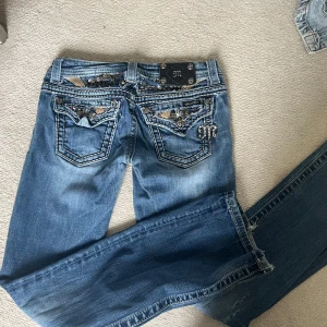 Miss Me jeans med paljettdetaljer - Snygga blå Miss Me jeans med coola paljettdetaljer och broderier på bakfickorna. Tydliga kontrastsömmar, dekorativa nitar och en unik läderpatch med metall-logga bak. Klassisk femficksmodell i stretchig jeanskvalitet. Perfekta för dig som gillar statement-plagg. Lite tecken på användning men annars superbra skick