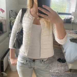 Vit stickad cardigan jacka - Säljer en söt vit stickad cardigan jacka med trekvartsärm och fina virkade detaljer. Jackan är öppen framtill och har ett luftigt, mönstrat stickat tyg som ger en fräsch och somrig vibe. Perfekt att slänga över ett linne eller klänning för en chill look.