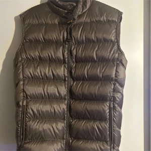 Brun dunväst från Parajumpers - Snygg brun dunväst från Parajumpers med quiltad design och hög krage. Västen har dragkedja framtill och två sidofickor med dragkedja. Märkets klassiska patch sitter på kragen. Perfekt för lager-på-lager under kyliga dagar.
