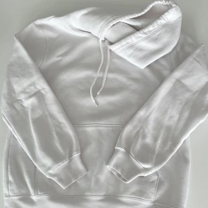 Vit hoodie från H&M, relaxed fit - Klassisk vit hoodie från H&M i relaxed fit. Tröjan har huva med snörning, magficka och ribbade muddar vid ärmslut och nederkant. Perfekt för en chill och stilren look. Tillverkad i mjuk bomullsmix som känns skön mot huden.