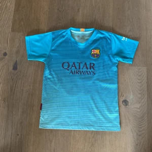 FC Barcelona Messi 10 bortatröja blå - Snygg FC Barcelona bortatröja med Messi 10-tryck. Tröjan är blå med tunna horisontella ränder, klubbmärke på bröstet och Qatar Airways som sponsor. Tillverkad i lätt och ventilerande polyester, perfekt för fotboll eller att bära som supporter.