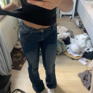 Blå bootcut jeans från DK Jeans - Säljer ett par blå lågmidjade bootcut jeans från DK Jeans med snyggt slitna detaljer och cool gul brodyr på bakfickorna. Jeansen har klassisk femficksdesign, låg midja och kontrastsömmar. Jag har sytt in de på sidorna vilket gör att det syns en tydlig söm utanför kanterna, men jag tycker det kan bidra till en snygg detalj. Det är även ett litet hål på benet som man kan se på sista bilden men ingen som syns och som går lätt och laga. Storlek XS/S.