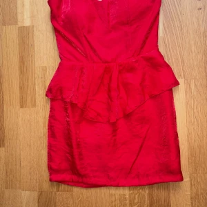 Röd kort klänning från Bik Bok - Snygg röd kort klänning från Bik Bok med peplum-detalj i midjan och dragkedja bak. Klänningen har en glansig finish och figurnära passform, perfekt för dig som vill sticka ut. Materialet känns lätt och följsamt.
