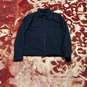 Mörkblå jacka från Traveler - Säljer en stilren mörkblå jacka från Traveler. Jackan har en dragkedja framtill och två bröstfickor med knappar. Den är designad för att vara stretchig, vattenavvisande och vindtät. Perfekt för dig som är på språng och vill ha en funktionell men snygg look.