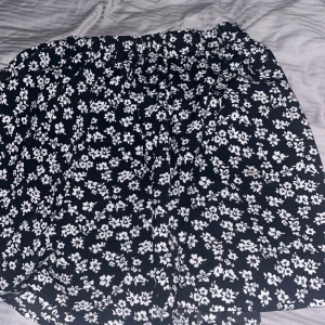 Svart blommig kjol från SHEIN - Svart kjol från SHEIN med vita blommor över hela tyget. Kjolen har en kort längd och resår i midjan för en bekväm passform. Perfekt för dig som gillar en söt och trendig stil.