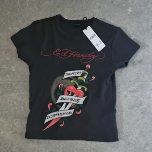 Ed Hardy t-shirt - Oanvänd Svart t-shirt från Ed Hardy med ikoniskt tatueringsinspirerat tryck på framsidan. Perfekt för dig som gillar streetstyle och edgy vibes. 