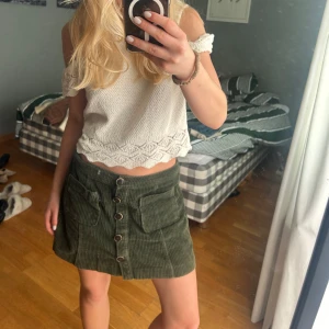 Grön manchesterkjol med knappar - Säljer en grön kort manchesterkjol med stora fickor framtill och snygga knappar längs hela framsidan. Kjolen har en cool retrovibe och är perfekt att styla med en croppad topp eller stickad tröja. Skön passform och riktigt trendig färg!