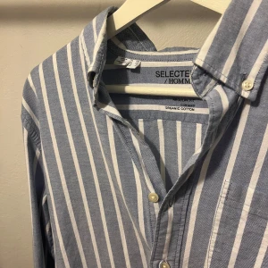 Blåvit randig skjorta från Selected Homme - Snygg blå och vit randig skjorta från Selected Homme i ekologisk bomull. Skjortan har klassisk krage, bröstficka och knäppning framtill. Regular fit och långa ärmar med manschett. Perfekt för en clean och stilren look.