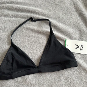 Svart trekantsbikini från SOC - Svart trekantsbikini från SOC med justerbara axelband och enkel knäppning i ryggen. Snygg och stilren modell i mjukt syntetmaterial som sitter skönt. Perfekt för stranden eller poolen. Storlek 158/164 som xxs.