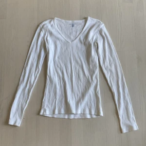 Vit ribbad långärmad tröja Brandy Melville strl S - Superskön vit långärmad tröja från Brandy Melville i ribbad bomull. Tröjan har v-ringning och sitter snyggt figurnära. Perfekt att styla med jeans eller kjol för en clean och enkel look. Endast använd någon gång